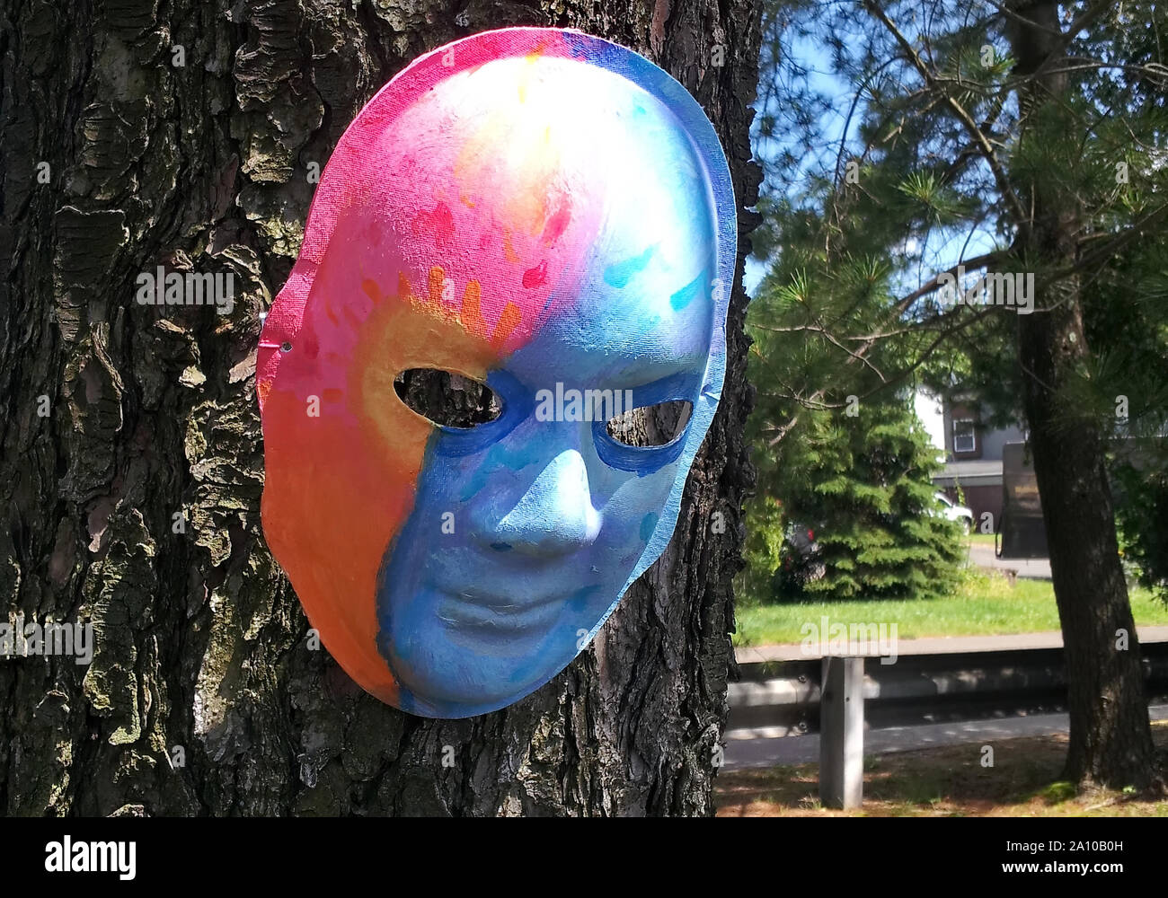 My kid`s artwork of a two face colored mask hanging on a tree. Symbolic of the duality of mans personification. Stock Photo